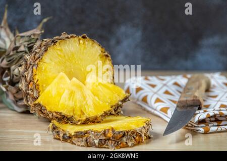 un ananas mûr coupé en deux, des tranches et des morceaux prêts à paquer. Fruits mûrs hachés par un couteau à manche en bois Banque D'Images