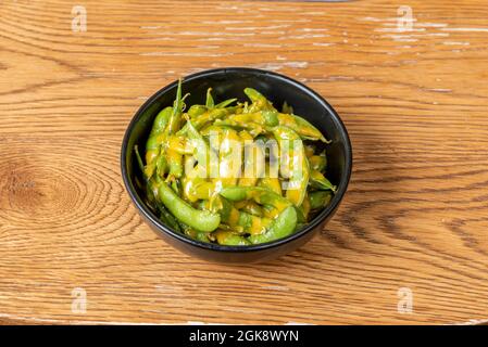 Edamame asiatique en gousse avec sauce au curry sur un bol noir et une table en chêne Banque D'Images