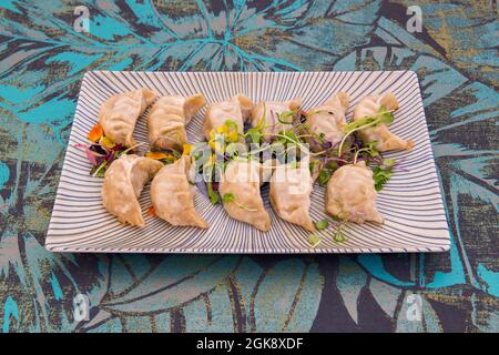 Grande portion de gyosas japonaises cuites sur le grill décorées de pousses et de fleurs comestibles sur une assiette blanche et bleue Banque D'Images