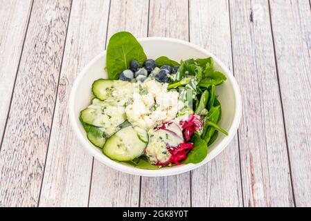 Salade de concombres, d'oignons rouges, de feta émietté, de bleuets et d'épinards sur un bol de livraison à domicile. Banque D'Images