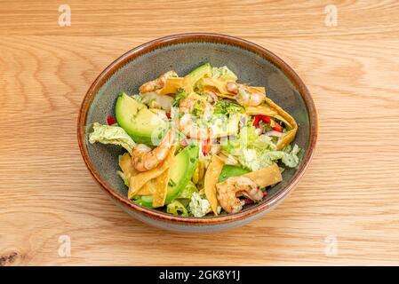 salade de crevettes incroyable, avocat, bandes de chips de maïs, laitue iceberg, beaucoup de persil et d'huile dans un bol gris à bord brun. Banque D'Images