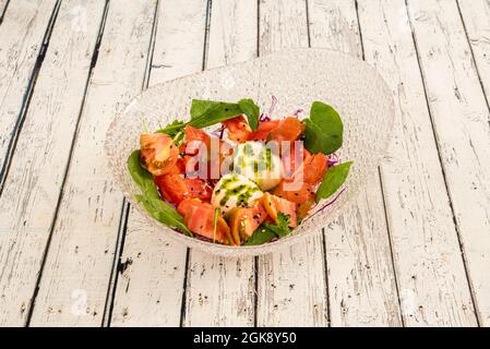 Bol en verre avec salade de tomates hachées, burrata en tranches et épinards sur fond blanc Banque D'Images
