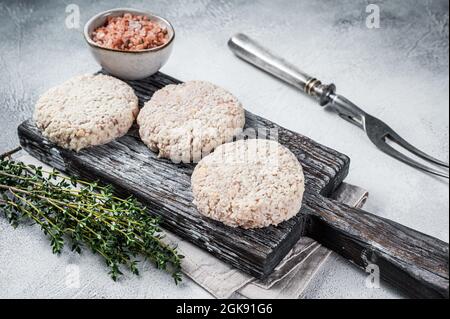 Côtelettes de patty de viande crue avec chapelure sur planche à découper en bois. Arrière-plan blanc. Vue de dessus Banque D'Images