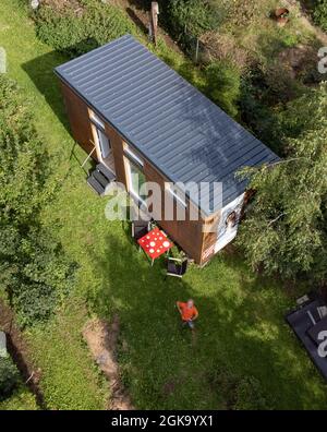 07 septembre 2021, Hessen, Schöneck-Kilianstädten: Uwe Christof se dresse devant sa petite Maison, située dans son jardin d'allotement (vue aérienne prise avec un drone). Depuis des années, le spécialiste INFORMATIQUE de la retraite anticipée fait campagne pour ce qu'on appelle les petites maisons, essentiellement transportables qui, malgré leur faible encombrement, sont censées offrir à leurs habitants tout ce dont ils ont besoin pour vivre et peuvent être mis en place partout où cela est permis et les propriétaires aiment cela. À Hesse aussi, cela pourrait se transformer en une forme de vie pour l'avenir. (À dpa 'petites maisons avec un grand avenir? Petit Ho Banque D'Images