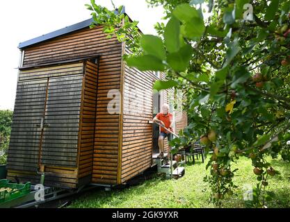 07 septembre 2021, Hessen, Schöneck-Kilianstädten: Uwe Christof se dresse à l'entrée de sa petite maison, qui est située dans son jardin d'allotement. Depuis des années, le spécialiste INFORMATIQUE de la retraite anticipée fait campagne pour ce qu'on appelle les petites maisons, essentiellement transportables qui, malgré leur faible encombrement, sont censées offrir à leurs habitants tout ce dont ils ont besoin pour vivre et peuvent être mis en place partout où cela est permis et les propriétaires aiment cela. À Hesse aussi, cela pourrait se transformer en une forme de vie pour l'avenir. (À dpa 'petites maisons avec un grand avenir? Petites maisons également en demande à Hes Banque D'Images