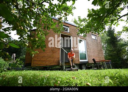 07 septembre 2021, Hessen, Schöneck-Kilianstädten: Uwe Christof est assis à l'entrée de sa petite maison, qui est située dans son jardin d'allotement. Depuis des années, le spécialiste INFORMATIQUE de la retraite anticipée fait campagne pour ce qu'on appelle les petites maisons, essentiellement transportables qui, malgré leur faible encombrement, sont censées offrir à leurs habitants tout ce dont ils ont besoin pour vivre et peuvent être mis en place partout où cela est permis et les propriétaires aiment cela. À Hesse aussi, cela pourrait se transformer en une forme de vie pour l'avenir. (À dpa 'petites maisons avec un grand avenir? Les petites maisons aussi en demande Banque D'Images