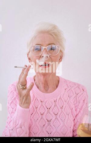 Ancienne femme élégante et ancienne fumant une cigarette avec un verre de vin blanc. Mauvaise habitude, concept de dépendance Banque D'Images