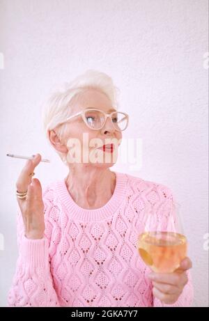 Ancienne femme élégante et ancienne fumant une cigarette avec un verre de vin blanc. Mauvaise habitude, concept de dépendance Banque D'Images