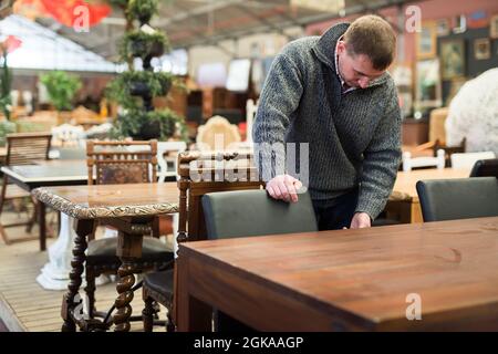 L'homme choisit une table en bois dans un magasin de meubles Banque D'Images