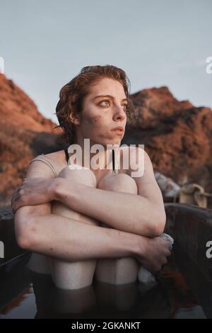 Jeune femme dépressive assise dans un bain sale et regardant le coucher de soleil dans le désert Banque D'Images