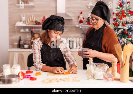 Grand-mère enseignant à la petite-fille comment préparer des biscuits faits maison en utilisant la forme de cuisson dans la cuisine décorée culinaire de Noël. Bonne famille en appréciant les vacances de noël ensemble cuisine dessert Banque D'Images