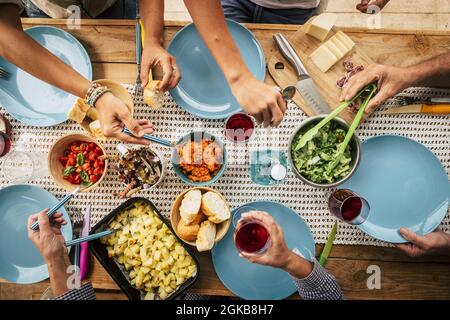 Groupe d'amis qui mangent avec un verre de vin sur la table à manger. Mains prenant les aliments du bol sur l'assiette. Groupe de personnes appréciant la variété de la nourriture et Banque D'Images