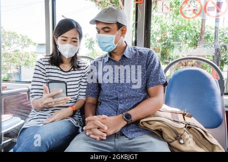 couple à bord d'un bus public ensemble portant un masque facial Banque D'Images