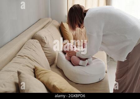 Jeune femme se pliant sur un canapé avec un bébé en pleurs mignon et essayant de la calmer Banque D'Images