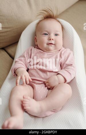 Adorable bébé dans des vêtements roses se détendant dans un petit lit blanc doux devant l'appareil photo Banque D'Images