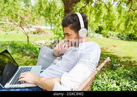 Travailleur indépendant attentionné travaillant sur un ordinateur portable dans le jardin comme bureau à domicile Banque D'Images