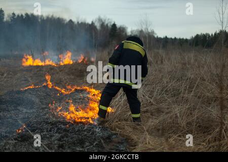 Un pompier éteint l'herbe sèche. Un pompier lutte contre un incendie dans une zone ouverte. Mesures de secours contre les flammes. Une catastrophe écologique brûlée Banque D'Images