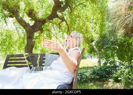 Bonne femme âgée qui fait un appel téléphonique avec un smartphone dans le jardin en été Banque D'Images