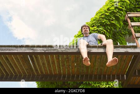 Jeune homme indépendant assis sur une jetée au bord du lac en été en vacances Banque D'Images