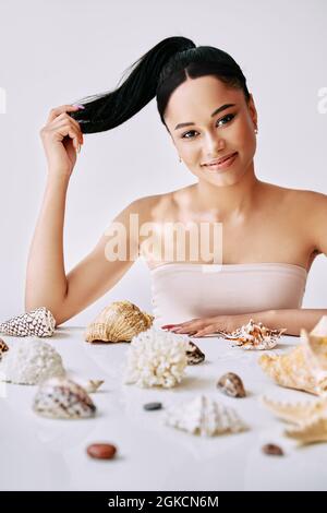 Souriante jolie femme afro avec différentes coquillages sur fond blanc. Portrait de femme de beauté