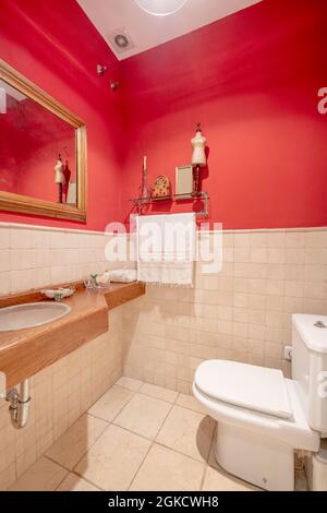 toilettes avec mur supérieur rouge et carrelage en marbre, miroir avec cadre doré et mains courantes avec comptoir en chêne Banque D'Images