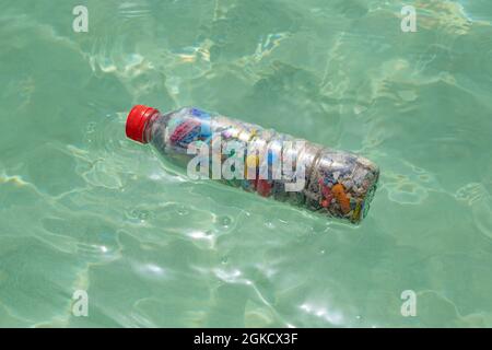 Bouteille remplie de microplastiques reposant sur de l'eau de mer Banque D'Images