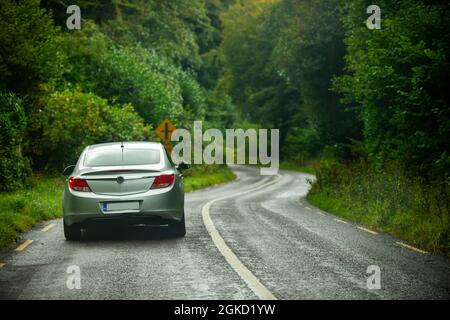 Véhicule gris moderne qui roule sur une route bordée d'arbres irlandais par un jour pluvieux typique Banque D'Images