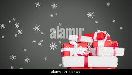 Image numérique des flocons de neige tombant sur des cadeaux de noël sur fond gris Banque D'Images