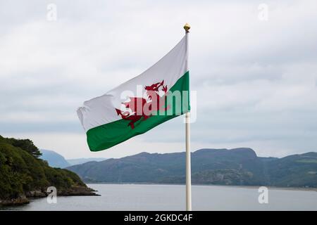 Le drapeau national gallois, le dragon rouge (y Ddraig Goch) volant sur la côte ouest du pays de Galles avec des montagnes de Snowdonian en arrière-plan Banque D'Images