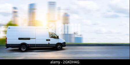 Un minibus blanc se déplace sur une route de la ville au coucher du soleil sur fond de paysage urbain. Banque D'Images