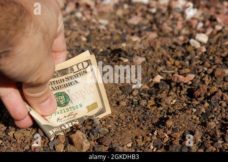 Main de l'homme plaçant le billet plié de dix dollars dans le sol. Investisseur d'argent immobilier, investissement foncier, concepts de projet de négociation Banque D'Images