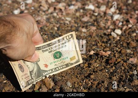 Main de l'homme plaçant une facture de dix dollars dans le sol. Investissement foncier, concepts de projet de négociation Banque D'Images