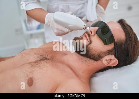 Jeune client spa dans des lunettes de sécurité pendant une procédure cosmétique Banque D'Images