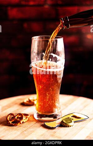 Processus de versement de la bière ambrée dans le verre sur un panneau de bois et des collations Banque D'Images