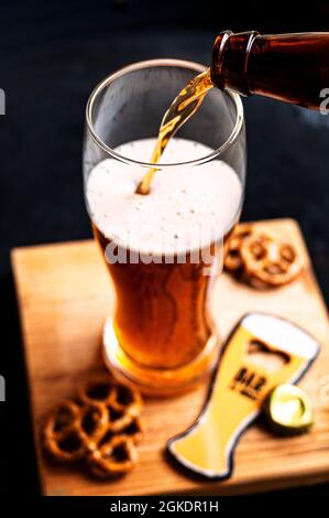 Processus de versement de la bière ambrée dans le verre sur un panneau de bois et des collations Banque D'Images