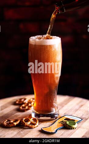 Processus de versement de la bière ambrée dans le verre sur un panneau de bois et des collations Banque D'Images