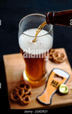 Processus de versement de la bière ambrée dans le verre sur un panneau de bois et des collations Banque D'Images