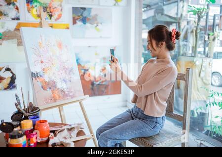 artiste asiatique prenant en photo sa propre peinture à l'aide d'un smartphone Banque D'Images