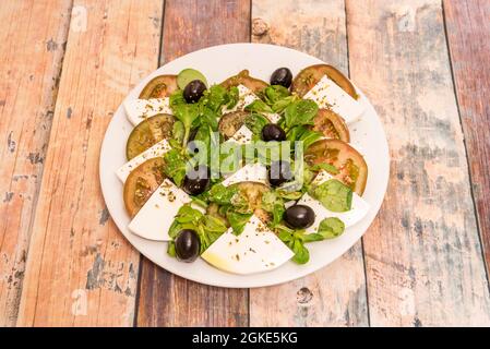 salade de fromage burrata aux olives noires, pousses de laitue d'agneau, tomates kumato et huile d'olive et origan sur table en bois Banque D'Images