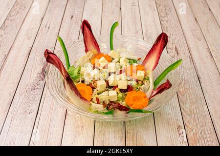 Spectaculaire salade de menthe poivrée avec carottes, poivrons, escarole, feta hachée et noix dans un bol en verre transparent. Banque D'Images