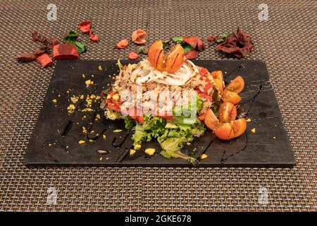 salade de laitue, poivrons piquillo rouges rôtis avec oignon et tomates cerises en morceaux avec poitrine de thon conservée sur plaque d'ardoise noire Banque D'Images