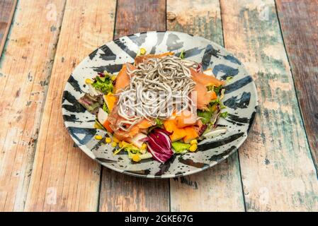 Salade de fruits de mer avec saumon fumé, surimi haché, anguilles pour bébés, laitue dans les pousses et maïs doux sur une assiette en bois Banque D'Images