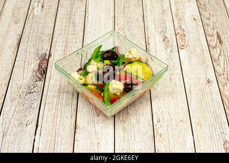 Bol en verre carré avec salade grecque d'olives noires, concombres, poivrons, oignon rouge et feta à l'huile d'olive. Banque D'Images