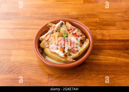 Salade de pommes de terre rôtie avec peau, bacon en morceaux, tomates en dés avec fromage à la crème sur pot d'argile Banque D'Images