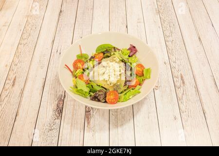 Salade de fromage de chèvre avec tomates cerises coupées en deux, laitue et huile d'olive dans un bol blanc Banque D'Images