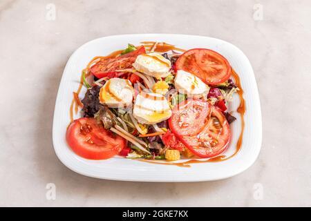 Délicieuse salade de fromage de chèvre avec sauce au curry douce, tranches de tomate, pousses de laitue, pousses de haricots, épis de maïs en saumure sur plaque en porcelaine blanche Banque D'Images