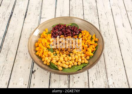 Salade avec du bœuf râpé, des pois chiches cuits, des carottes et de la citrouille hachées, des betteraves rouges coupées en dés et un lit d'épinards Banque D'Images