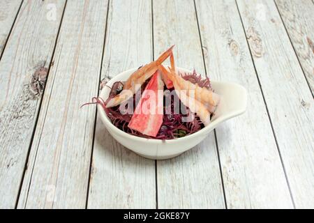 Salade d'algues mélangées avec surimi et crevettes cuites dans un petit bol blanc sur une table blanche. Banque D'Images