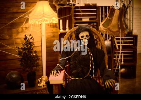 squelette effrayant de femme vêtue de cape noire est assis dans la chaise en soirée sur halloween Banque D'Images