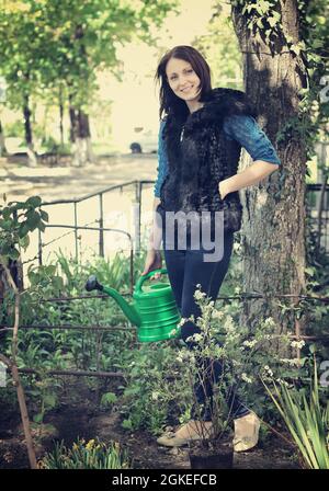 Souriante femme habillée dans la cour jardinage eaux fleurs et s'occupe Banque D'Images